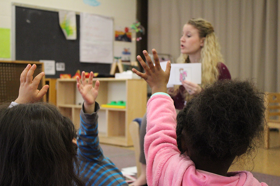 Children raise their hands while a teacher presents.